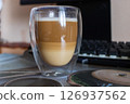 Layered Latte Macchiato in a Double-Walled Glass on a Desk 126937562