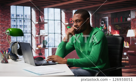Black man doing remote work feeling uneasy and anxious at desk, shaking his legs and being jittery due to task completion and deadline. Freelancer working under pressure, anxiety. Camera B. 126938051
