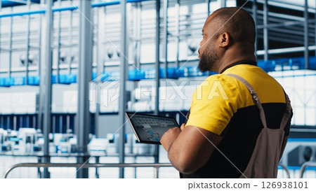 Industry 4.0 industrial plant expert designs new robotic machines using CAD program on tablet. Africna american man in smart factory using device to do tooling for automation equipment, camera A Industry 4.0 industrial plant expert designs new robotic machines using CAD program on tablet. Africna american man in smart factory using device to do tooling for automation equipment, camera A 126938101