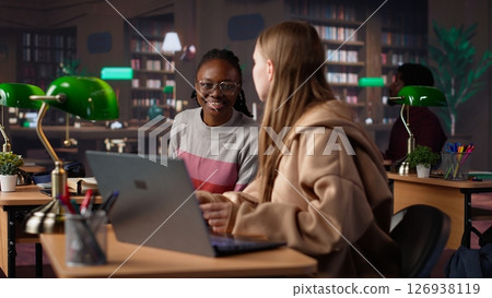 Female student reading and writing detailed notes for an exam, studying political science for upcoming lecture in a library setting at the university. Young adult consults a colleague. Camera A. Female student reading and writing detailed notes for an exam, studying political science for upcoming lecture in a library setting at the university. Young adult consults a colleague. Camera A. 126938119