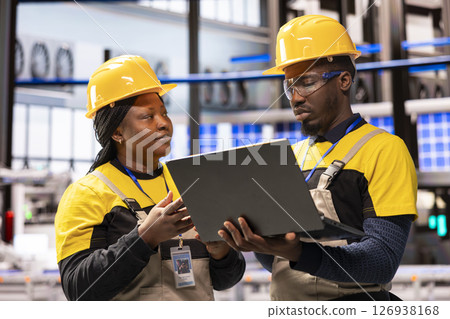 In smart manufacturing plant, african american engineers supervise industrial automation system using laptop. The automated factory features conveyor belts, robotic arms and optimized assembly lines. In smart manufacturing plant, african american engineers supervise industrial automation system using laptop. The automated factory features conveyor belts, robotic arms and optimized assembly lines. 126938168