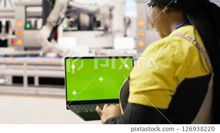 Engineer in photovoltaics factory using chroma key laptop to look at system performance metrics. Worker in industry 4.0 plant using green screen mockup notebook to track energy production, camera B Engineer in photovoltaics factory using chroma key laptop to look at system performance metrics. Worker in industry 4.0 plant using green screen mockup notebook to track energy production, camera B 126938220