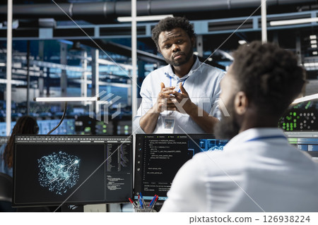 Server farm manager supervising engineer looking at data analysis graph to reduce failures. Data center team leader overseeing worker looking at AI visualization dashboard to pinpoint gear glitches 126938224