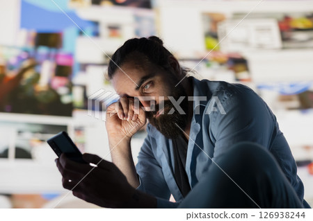 Distressed man suffers from social anxiety damage due to obsessive social media use. Young adult overwhelmed by excessive information and overload or cyberbullying affecting his self esteem. 126938244