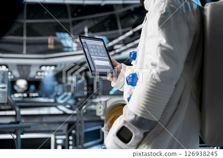 Close up of astronaut using tablet to view spacecraft analytics during scientific mission. Spaceship crew member in spacesuit looking at orbital navigation data on device during planetary exploration Close up of astronaut using tablet to view spacecraft analytics during scientific mission. Spaceship crew member in spacesuit looking at orbital navigation data on device during planetary exploration 126938245
