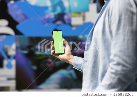 Male influencer holds phone with chroma key screen for online presence, using his imagination and storytelling skills to connect with followers and boost online engagement. Modern web design. Male influencer holds phone with chroma key screen for online presence, using his imagination and storytelling skills to connect with followers and boost online engagement. Modern web design. 126938263