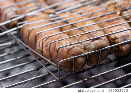 Close up sausages grilling in metal basket over hot coals Close up sausages grilling in metal basket over hot coals 126938550