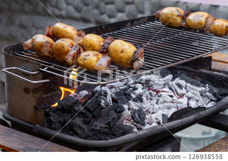 Grilling potatoes and bacon skewers on a charcoal barbecue grill Grilling potatoes and bacon skewers on a charcoal barbecue grill 126938558