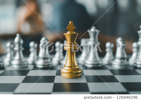 A golden chess king stands prominently on a chessboard surrounded by silver pieces, symbolizing strategy and leadership. 126940296