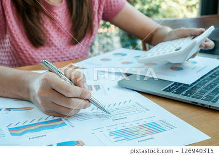 Close-up of a woman reviewing financial charts and using a calculator, highlighting business analysis and strategic planning. 126940315