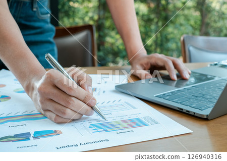 Close-up of hands working on financial charts and graphs with a laptop, showcasing business analysis and data management. 126940316