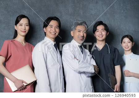Image of a cool gray-haired doctor and multiple other doctors smiling and looking at the camera 126940593