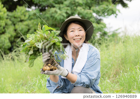 Woman growing potatoes in the field. Image of a farmer or agricultural worker. Close-up of a woman looking at the camera. Woman growing potatoes in the field. Image of a farmer or agricultural worker. Close-up of a woman looking at the camera. 126940889