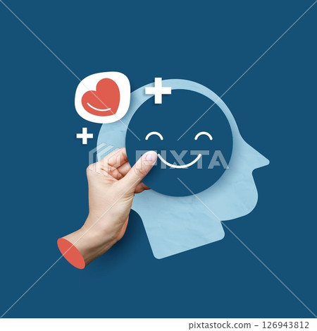 Medical concepts. hand holding happy face icon in front of head silhouette, symbolizing mental health, positivity, self-care, and emotional well-being on blue background. 126943812
