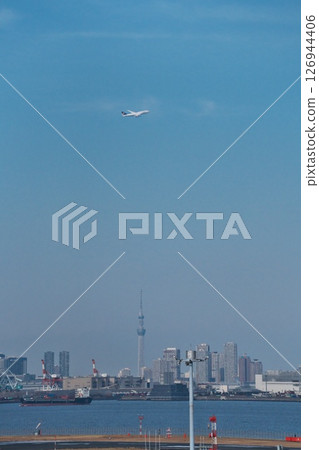 A German Lufthansa passenger plane takes off from runway C at Haneda Airport and flies over the Skytree, shining against the blue sky. 126944406