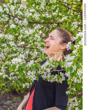 Young woman sneezes in the park against the background of a flowering tree. Allergy to pollen concept. 126944499