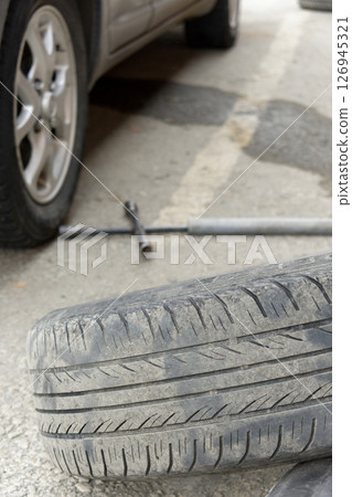 Car tire replacement on the side of the road. A flat tire is on the ground next to it 126945321