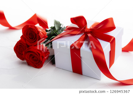 A gift box with a red ribbon and a bouquet of red roses A gift box with a red ribbon and a bouquet of red roses 126945367