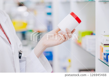 Close up Doctor Pharmacist hand holding medicine pills box from drugs shelf in drug store 126945488