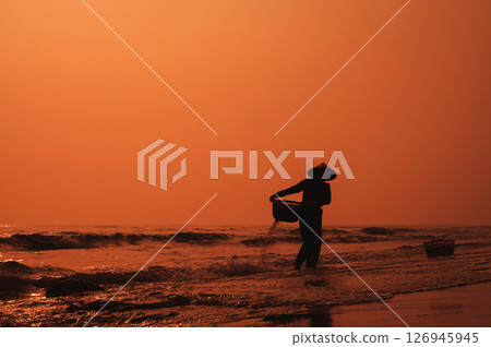 Silhouette of a Vietnamese woman in a straw hat on beach of sea in a fishing village in morning at sunrise in Vietnam 126945945