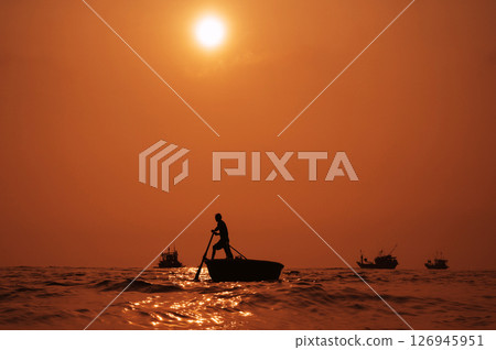 Silhouette of a Vietnamese male fisherman on a round basket boat in the sea in a fishing village in morning at sunrise in Vietnam Silhouette of a Vietnamese male fisherman on a round basket boat in the sea in a fishing village in morning at sunrise in Vietnam 126945951