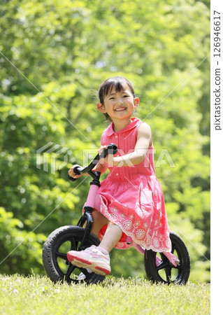 A girl riding a bicycle in a park with fresh greenery A girl riding a bicycle in a park with fresh greenery 126946617