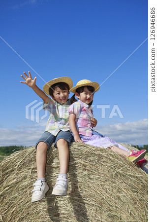 Brother and sister riding on a big hay roll 126946686