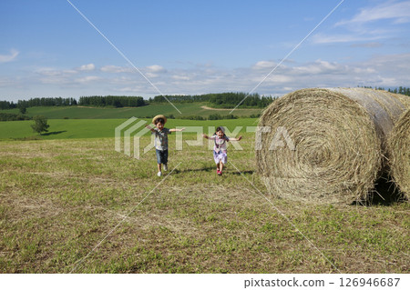 Brother and sister running next to a big hay roll 126946687