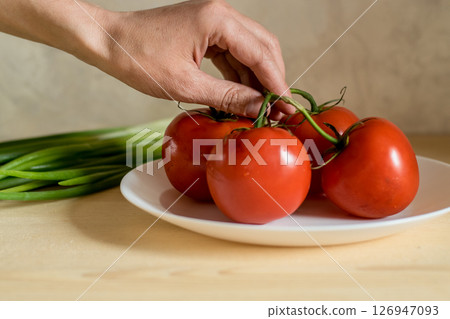 Close-up of a man's hand holding tomatoes by their green tails Close-up of a man's hand holding tomatoes by their green tails 126947093