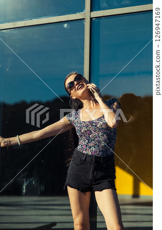 A young woman wearing shorts and a T-shirt stands near the transparent facade, holding a cell phone 126947169