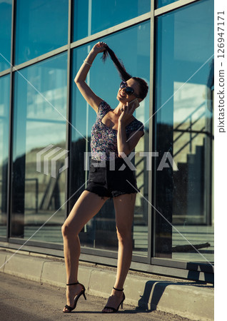 A young woman with glasses on her face smiles pleasantly as she talks on the phone outside a glass building A young woman with glasses on her face smiles pleasantly as she talks on the phone outside a glass building 126947171