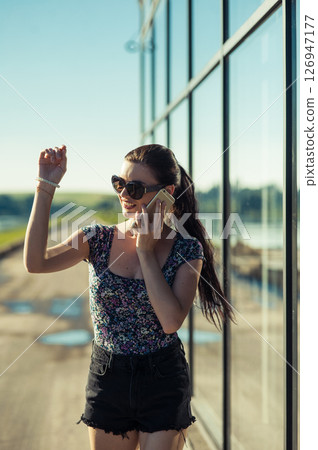 A young woman is talking intently near the transparent panels of the building. A young woman is talking intently near the transparent panels of the building. 126947177