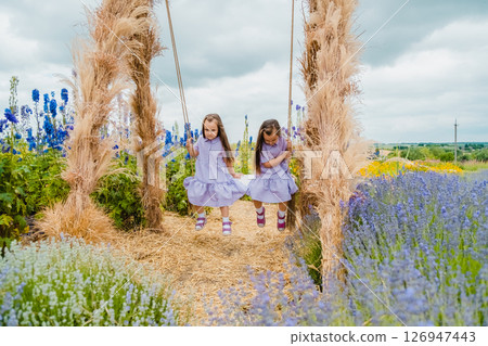 Twin girls swing on a big swing in the middle of a lavender field 126947443