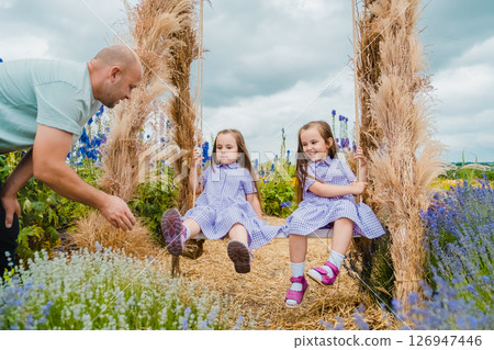 A young father and his daughters enjoy time together on a beautiful swing A young father and his daughters enjoy time together on a beautiful swing 126947446