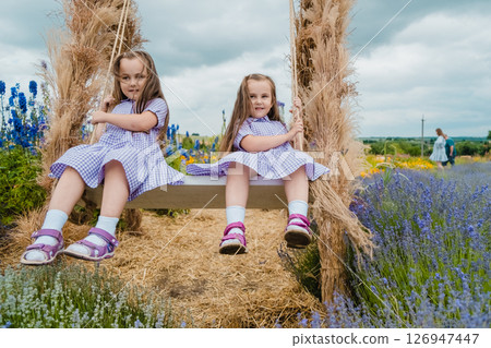 Cute girls are relaxing on a big swing in the middle of a lavender field. Cute girls are relaxing on a big swing in the middle of a lavender field. 126947447