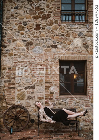 Woman Relaxing on Bench with Wine in Historic Setting 126947652
