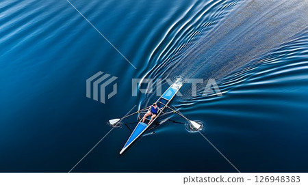 Solitary rower carving waves on glassy lake in quiet morning light 126948383