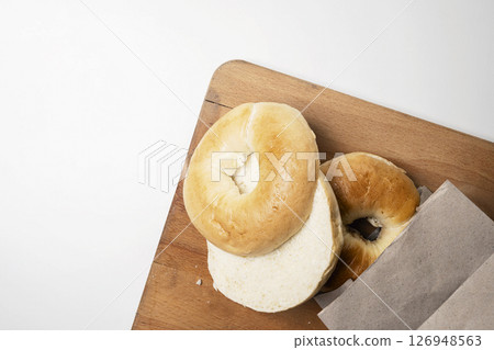 Closeup view of slice of bagel breads from brown paper bag on wooden board isolated over white background. Top view 126948563