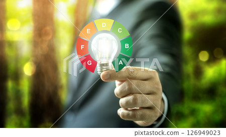Businessman holding bright light bulb with energy efficiency scale icon. Concept of energy efficiency Businessman holding bright light bulb with energy efficiency scale icon. Concept of energy efficiency 126949023