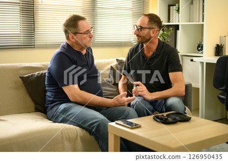 Adult son helping elderly father check blood sugar at home in a supportive health care moment. Adult son helping elderly father check blood sugar at home in a supportive health care moment. 126950435