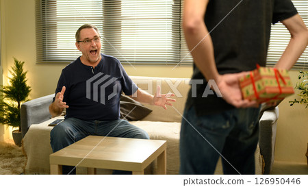 Excited father reacts with joy as son surprises him with a hidden gift at home. Father day concept 126950446
