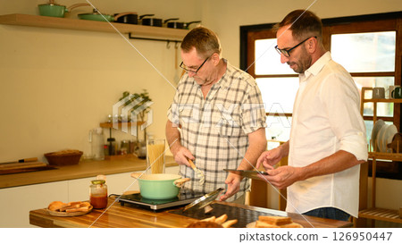 Smiling father and adult son preparing a pasta meal together in a cozy home kitchen. Father day concept Smiling father and adult son preparing a pasta meal together in a cozy home kitchen. Father day concept 126950447