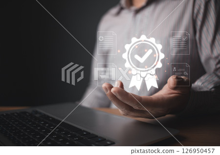 A person holds a glowing quality control badge hologram featuring a checkmark and surrounding digital document icons, symbolizing certification, standards, and reliable assurance in modern processes. 126950457