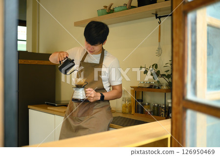 Man carefully pouring hot water into a coffee dripper in warm and inviting kitchen space. 126950469