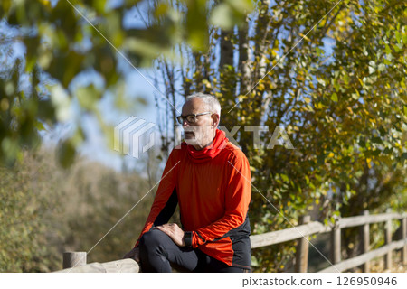 Senior man in bright orange hoodie resting on wooden fence 126950946