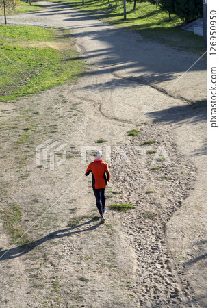 Senior man running on dirt trail from aerial perspective Senior man running on dirt trail from aerial perspective 126950950