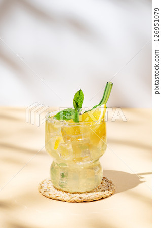 Fresh citrus lemonade mojito with lemon, mint and ice on a yellow background with shadows. Fresh citrus lemonade mojito with lemon, mint and ice on a yellow background with shadows. 126951079