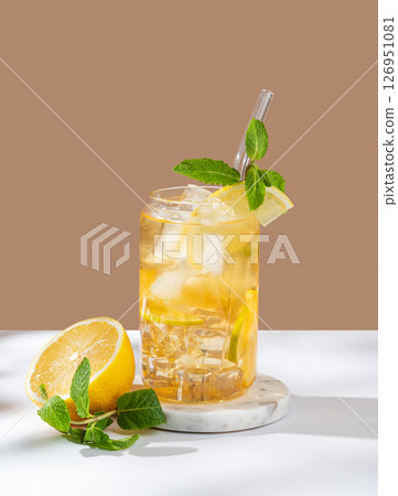 Iced tea with lemon and mint in a glass on a white beige background with citrus fruit and herbs. 126951081