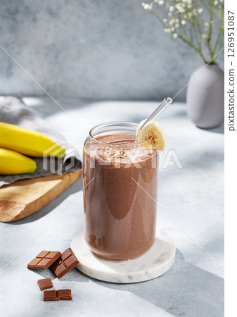 Chocolate smoothie with banana in a glass on a  blue background with fresh fruits and sunlight. 126951087