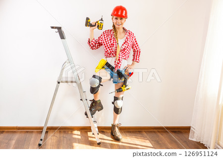 Woman wearing helmet, toolbelt on ladder 126951124